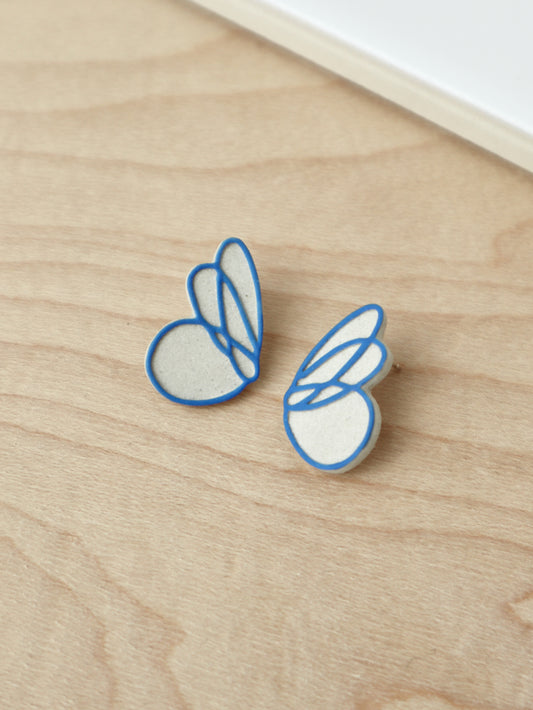 A pair of ceramic stud earrings, each shaped like a single butterfly wing with blue raised linework against warm stoneware.