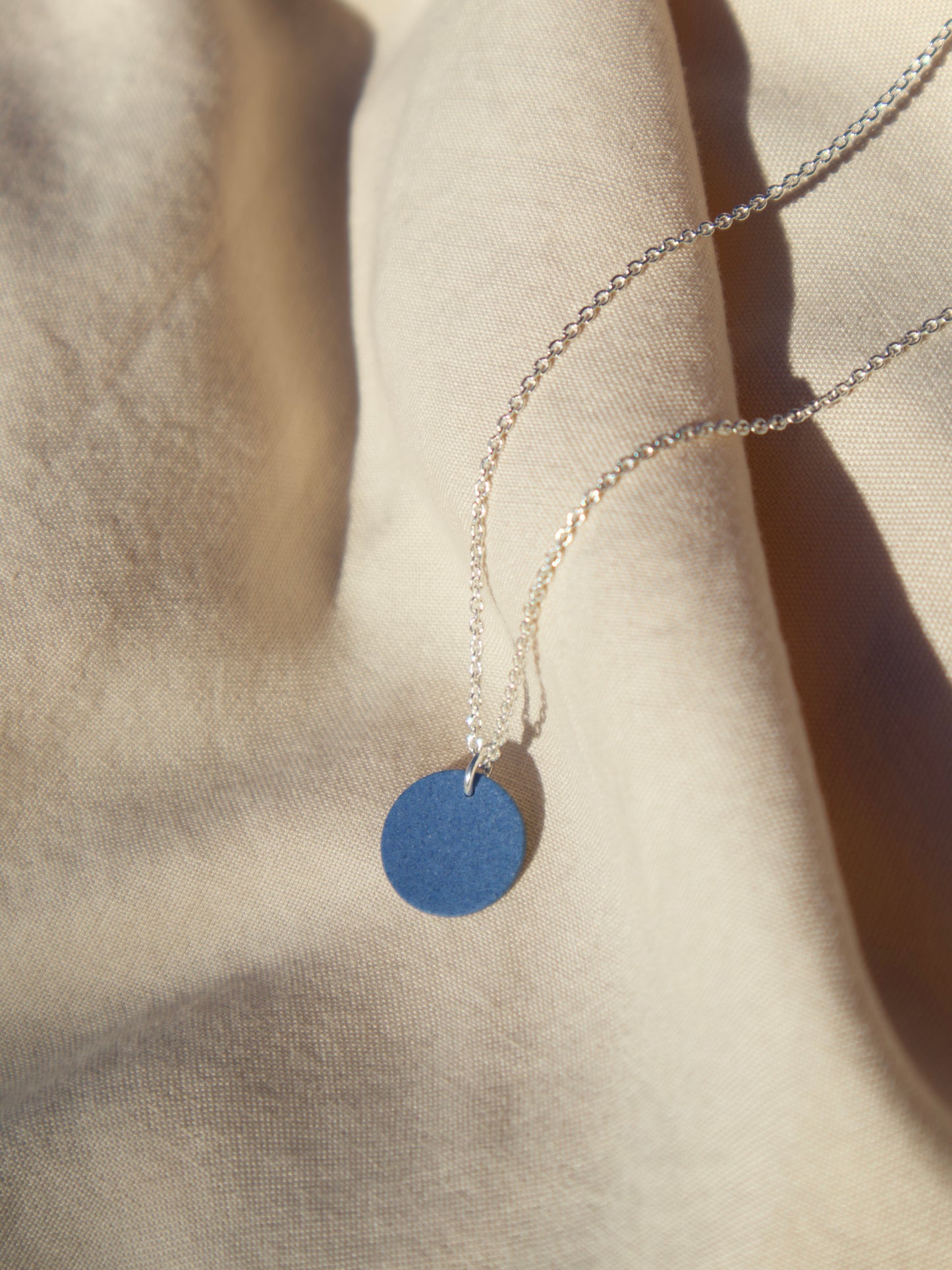 A sterling silver cable chain necklace with a cobalt blue circle pendant.