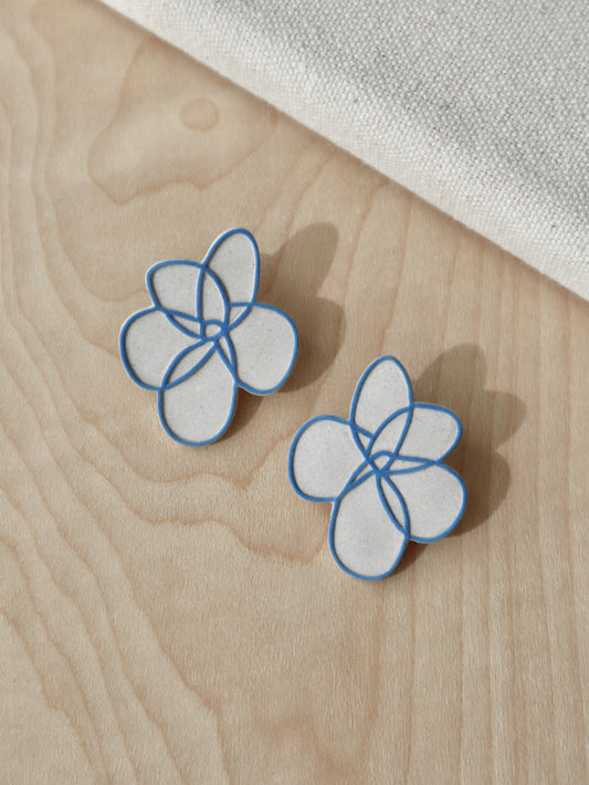 Handcrafted beige stoneware flower stud earrings with painted blue outline design.