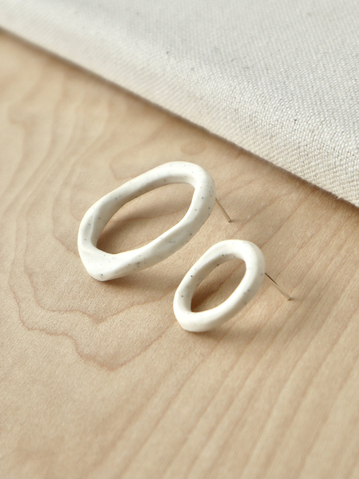 A pair of organic-shaped loop stud earrings made from speckled white porcelain.