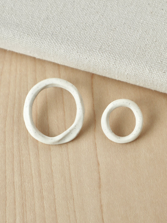 A pair of asymmetrical white porcelain loop stud earrings in two different sizes.