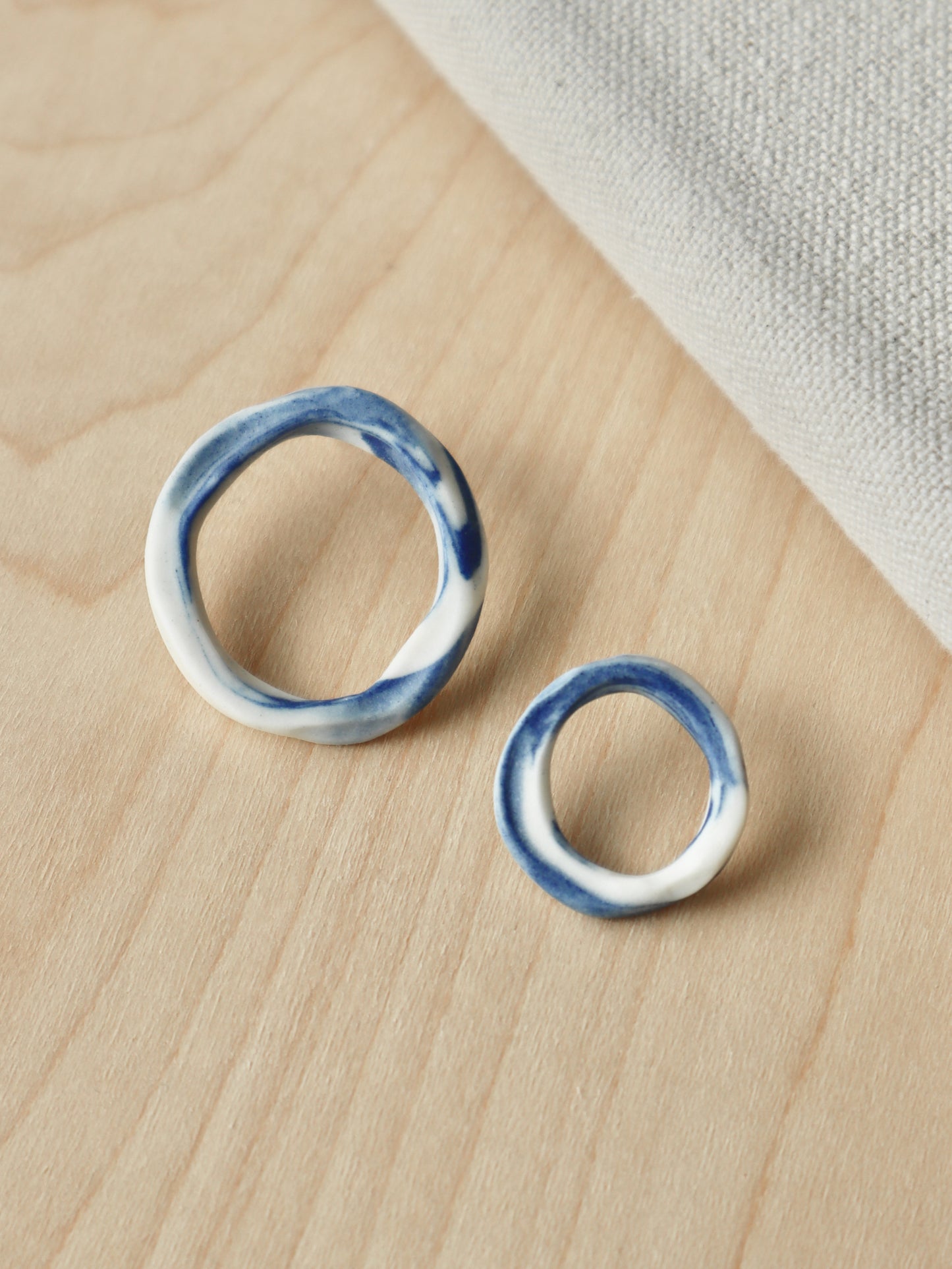 A pair of asymmetrical marbled cobalt and white porcelain loop stud earrings in two different sizes.