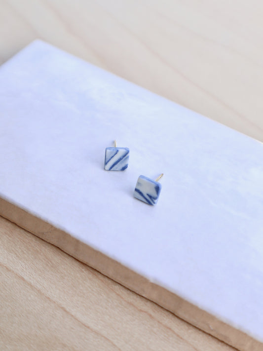 A pair of small square ceramic stud earrings in marbled cobalt blue and white porcelain.