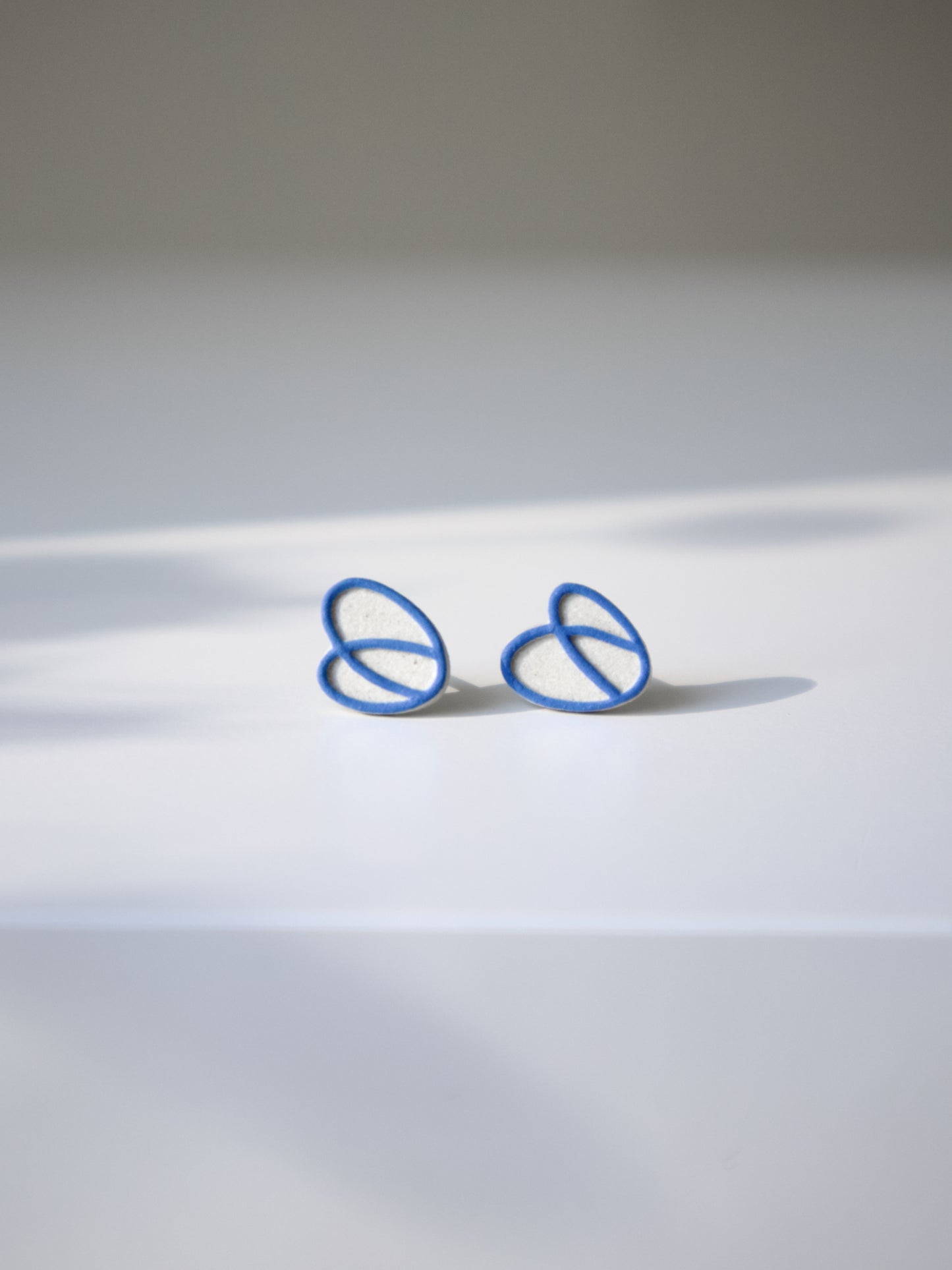 Natural stoneware stud earrings with an interlocking blue loop design.