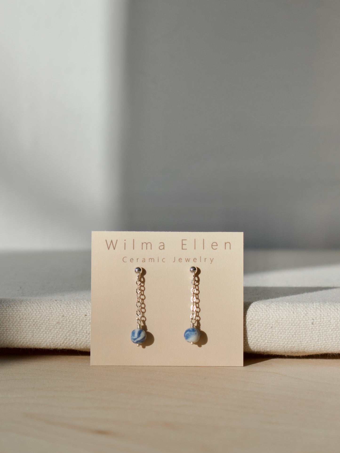 A pair of delicate drop earrings with marbled cobalt blue and white porcelain beads suspended from silver chain on ball studs.