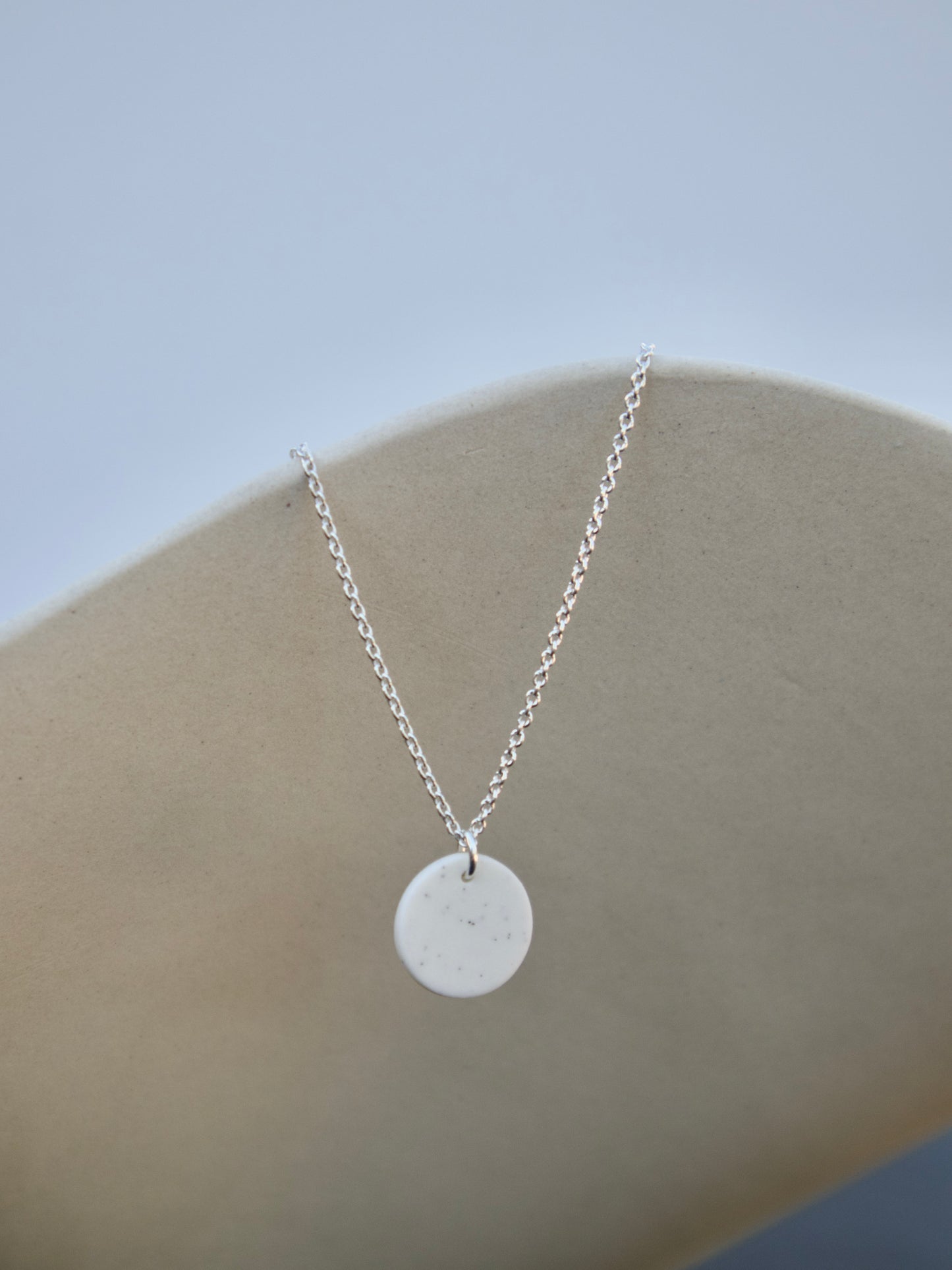 A sterling silver cable chain necklace with a white porcelain circle pendant.