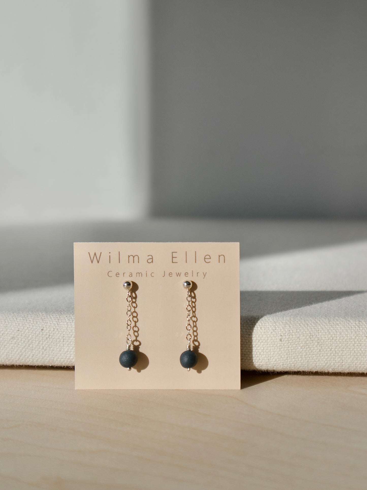 A pair of delicate drop earrings with midnight black porcelain beads suspended from silver chain on ball studs.