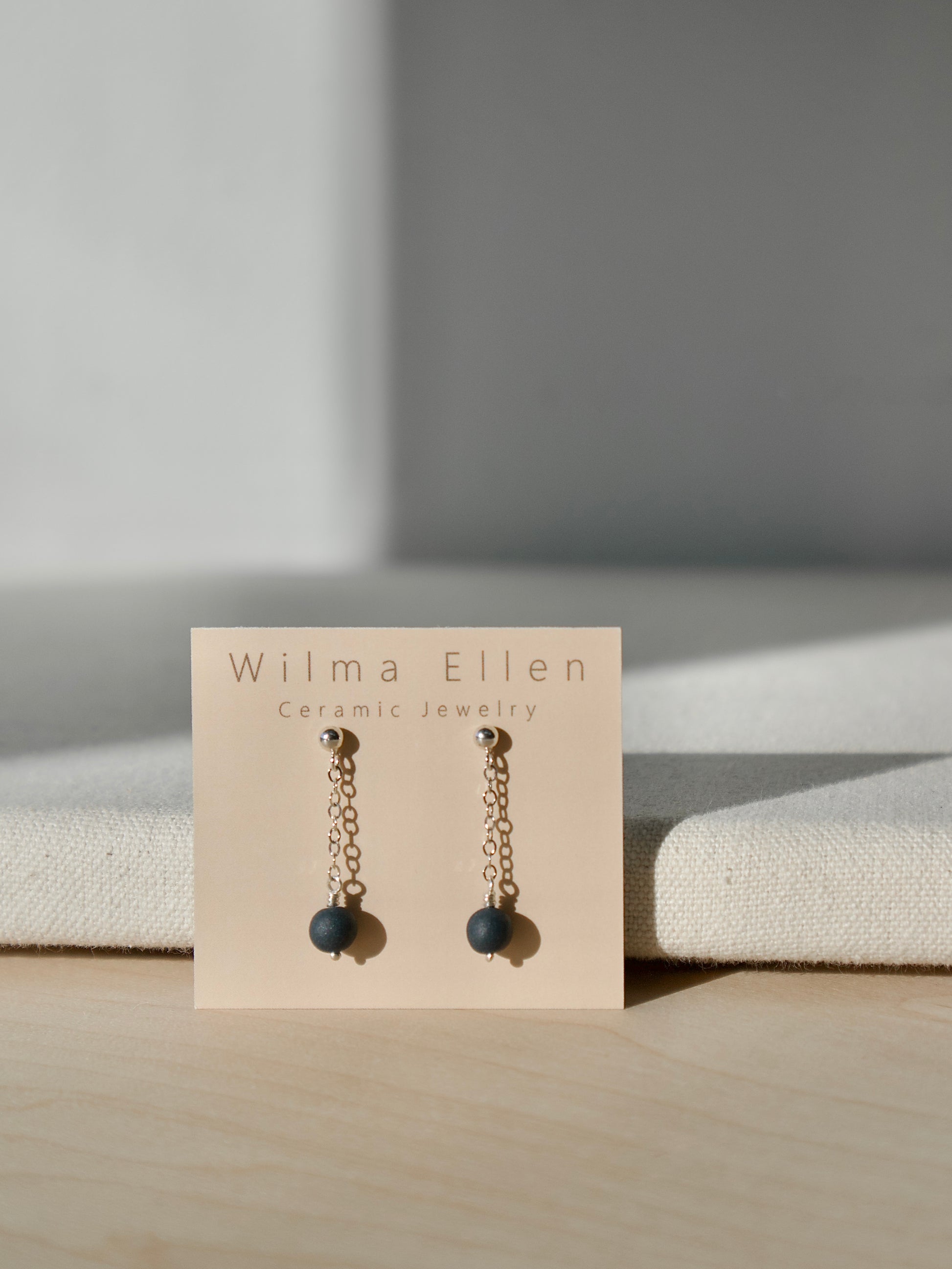 A pair of delicate drop earrings with midnight black porcelain beads suspended from silver chain on ball studs.