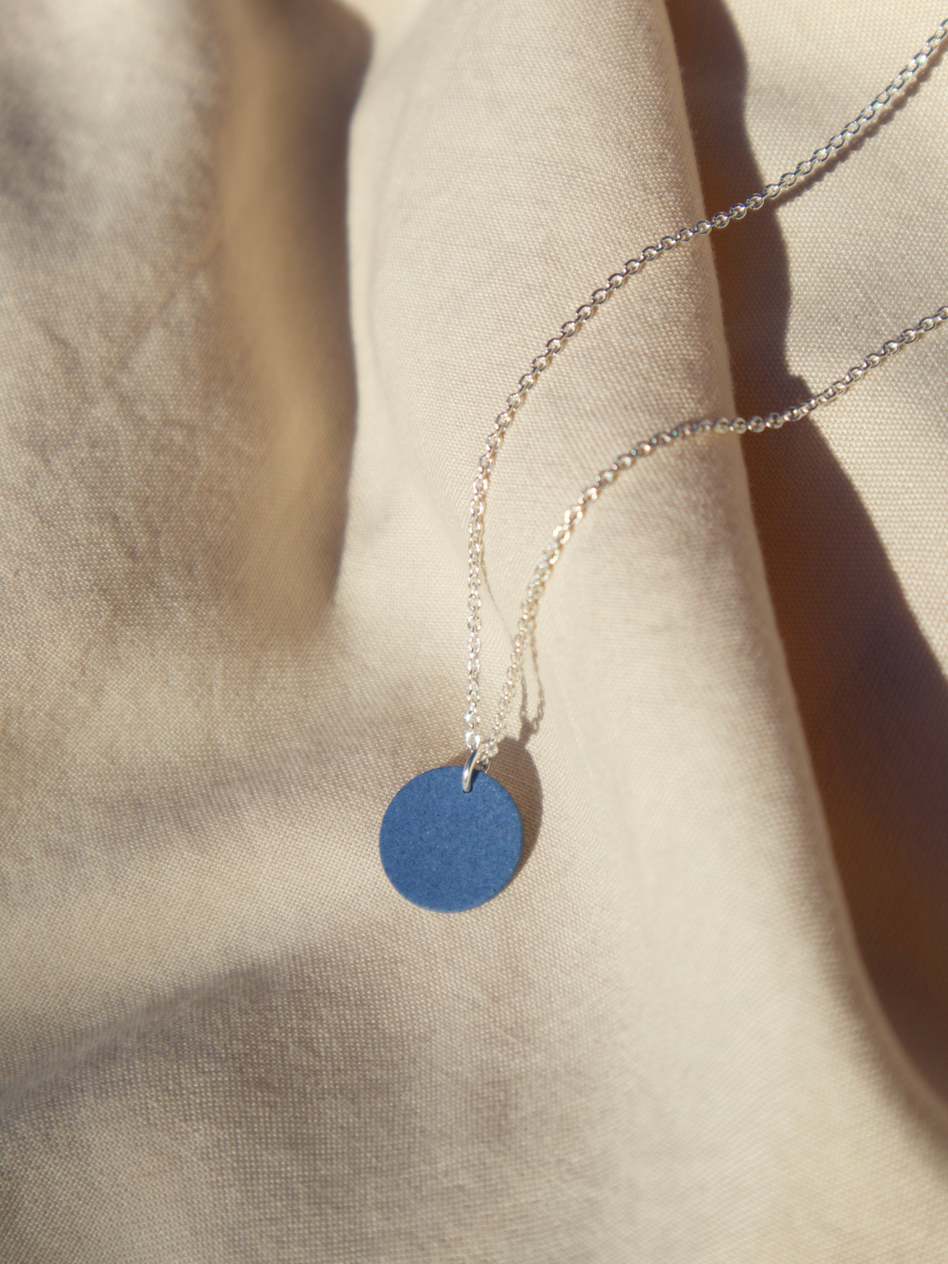 A sterling silver cable chain necklace with a cobalt blue circle pendant.