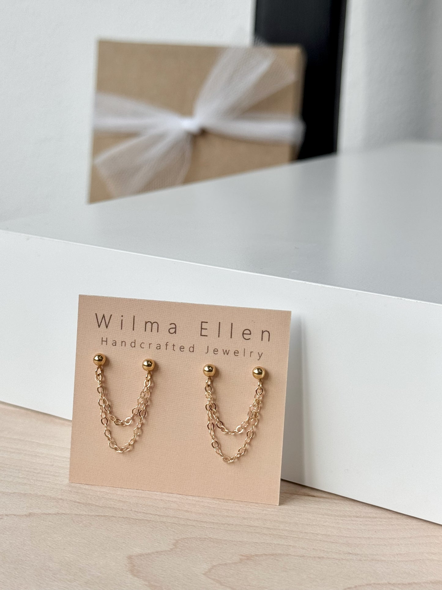 Gold ball stud earrings with two delicate chains draping between each pair of posts, designed for double piercings.