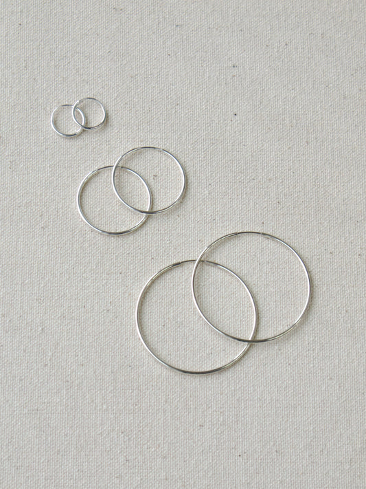 Three pairs of thin silver hoop earrings in different sizes. 