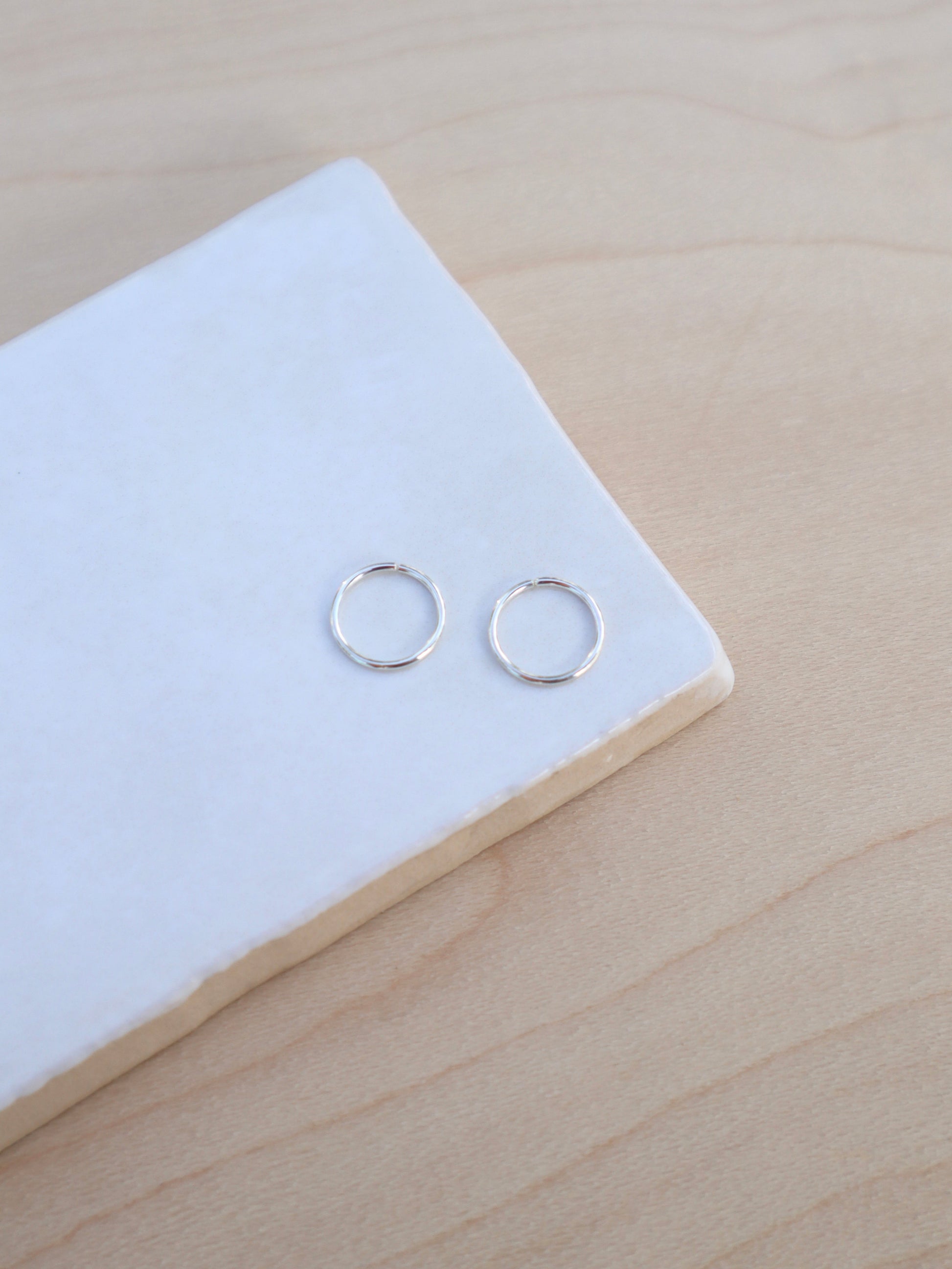 A pair of mini silver wire hoop earrings.