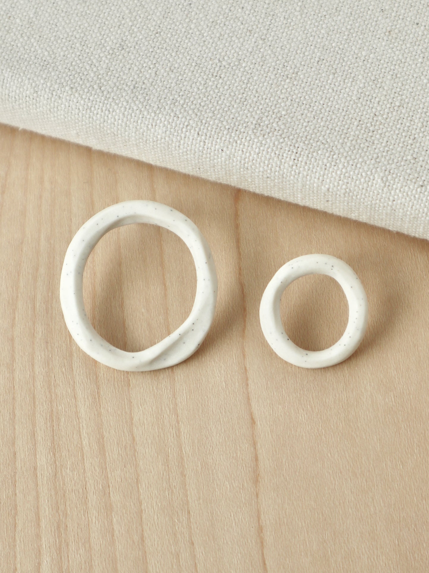 A pair of asymmetrical white porcelain loop stud earrings in two different sizes.
