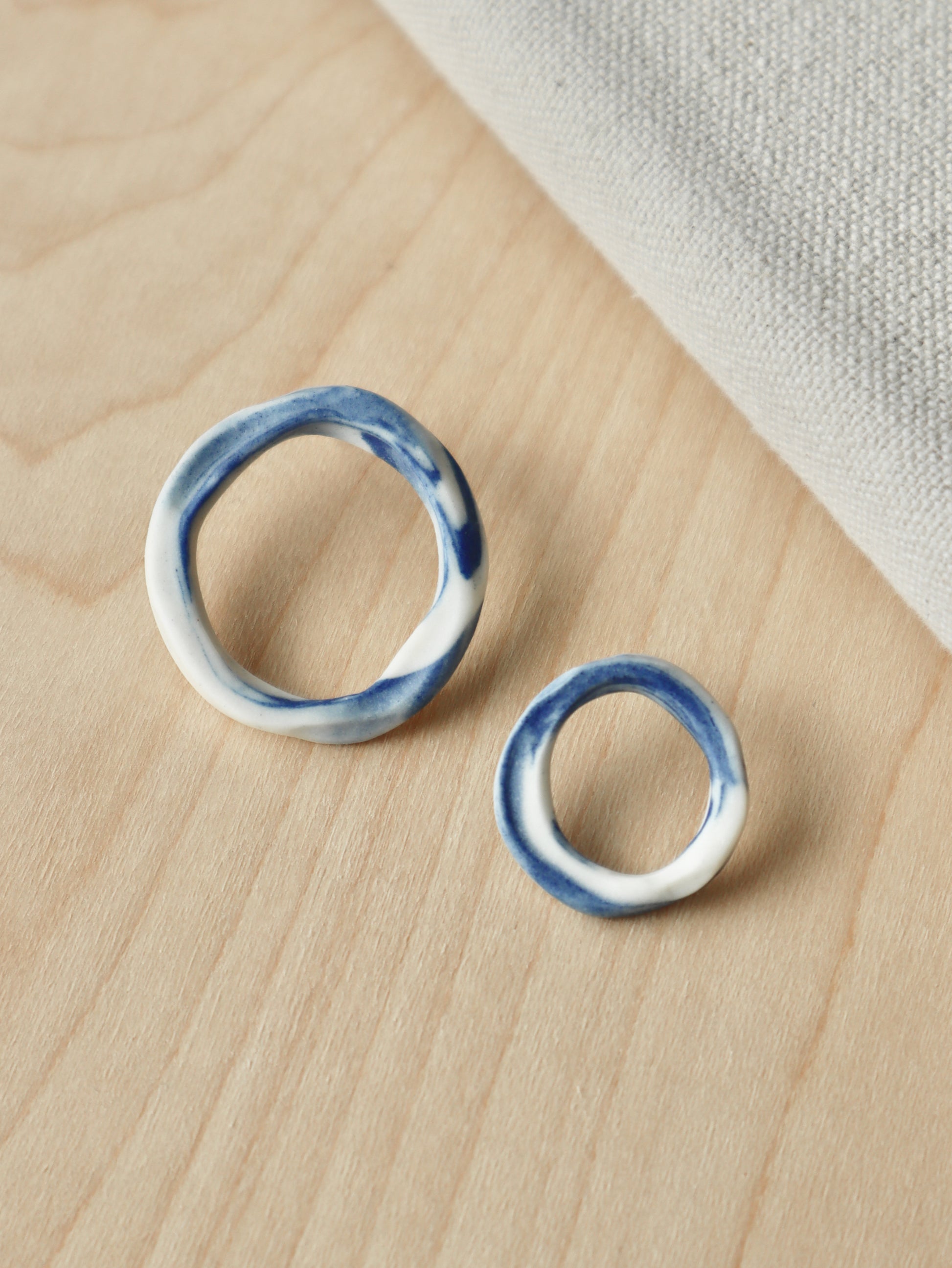 A pair of asymmetrical marbled cobalt and white porcelain loop stud earrings in two different sizes.