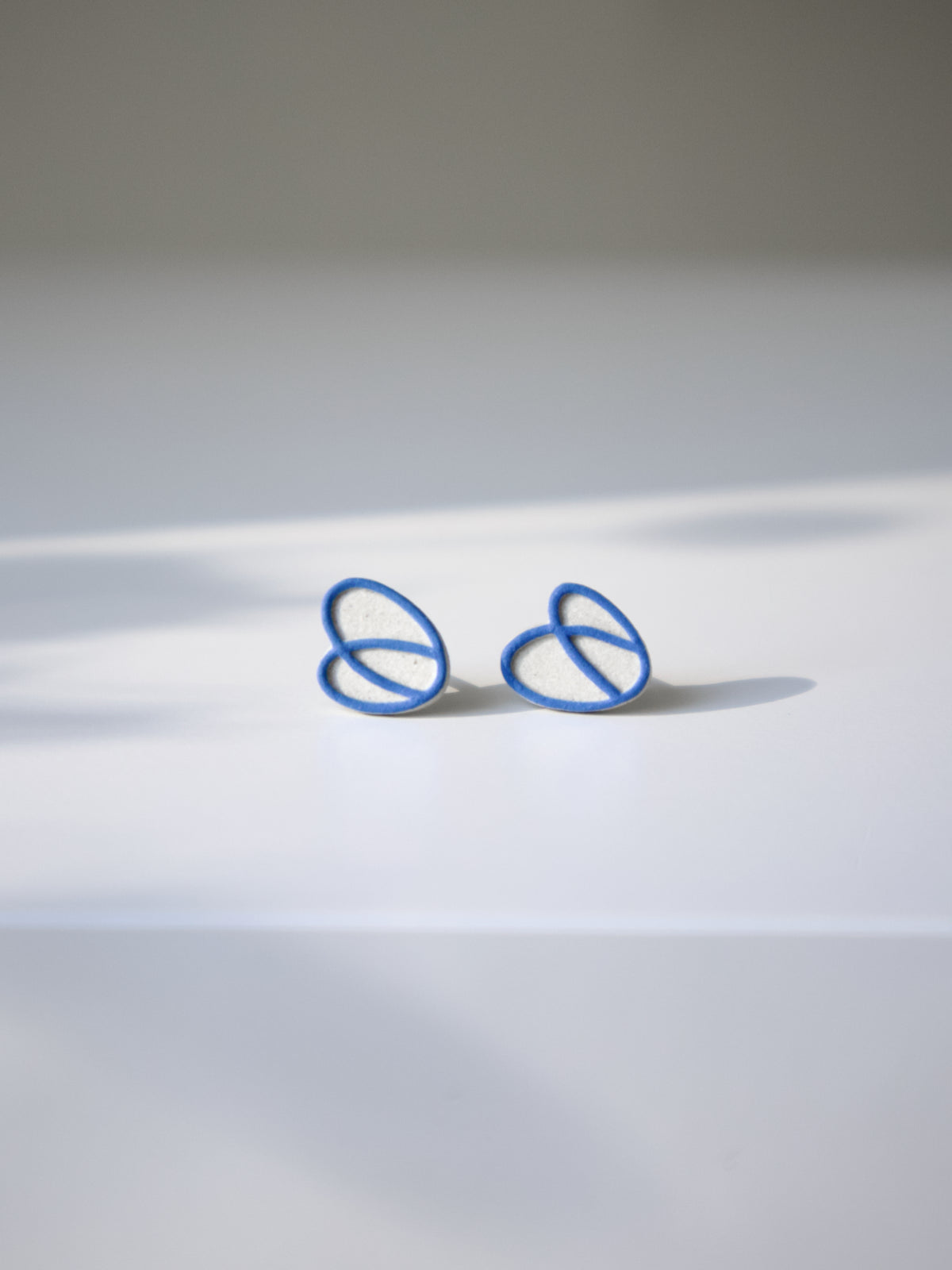 Natural stoneware stud earrings with an interlocking blue loop design.