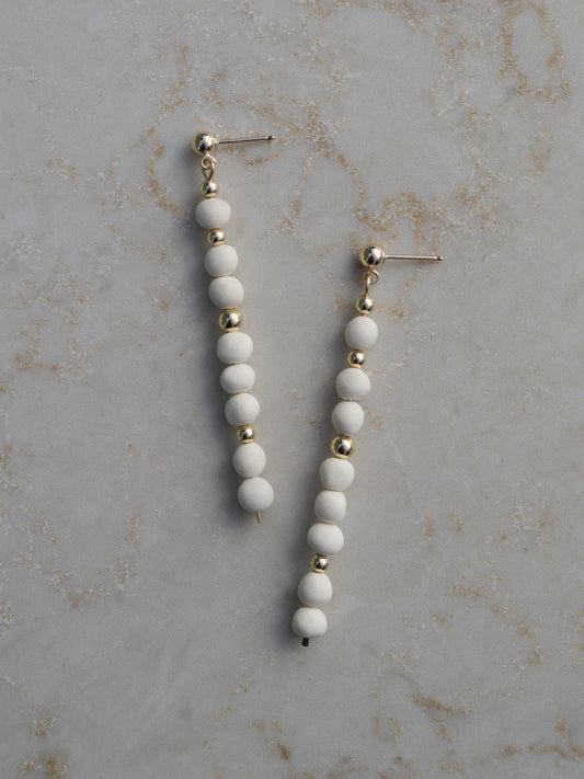 Long, dangle earrings made with stacked white porcelain and gold beads hanging on ball posts.