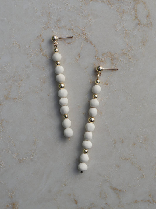 Long, dangle earrings made with stacked white porcelain and gold beads hanging on ball posts.